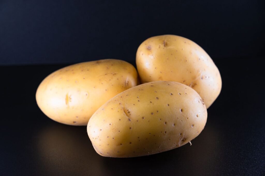 Studio shot of three fresh potatoes on a black surface, perfect for food photography.
