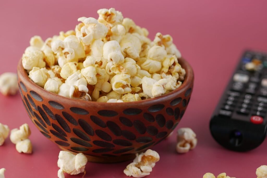 A vibrant close-up of popcorn in a decorative bowl beside a TV remote, ideal for snacks and entertainment themes.