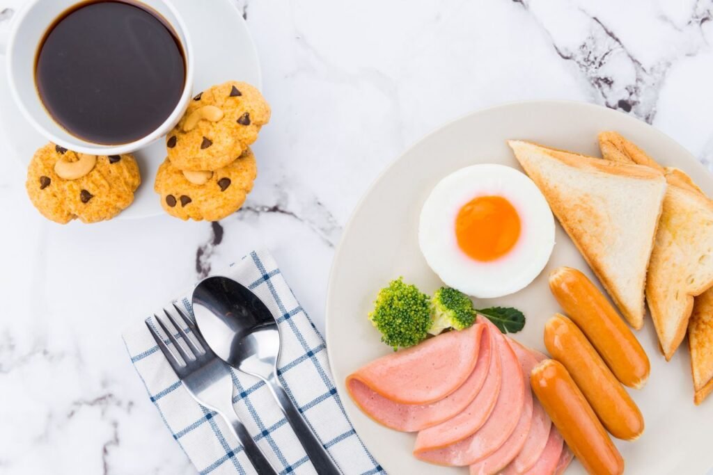 A hearty breakfast of toast, egg, sausages, and coffee on a marble surface.