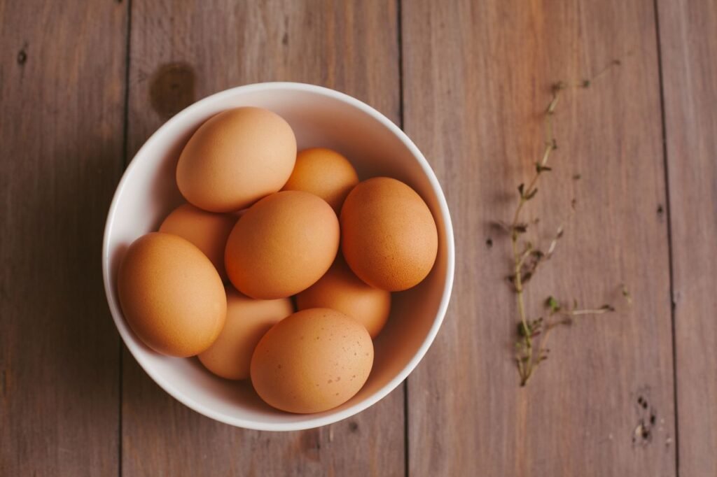 A close-up shot of fresh brown eggs in a white bowl on a rustic wooden table.