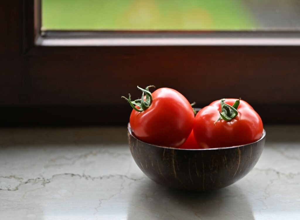 Vibrant red tomatoes in a rustic wooden bowl placed by a sunny window, perfect for illustrating organic freshness.