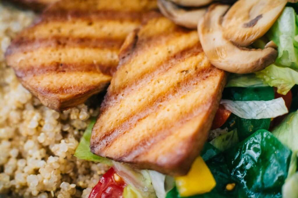 Close-up of grilled tofu, mushrooms, quinoa, and fresh vegetables in a vibrant salad.