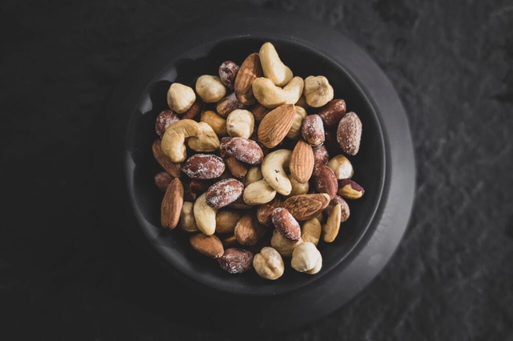 Top view of a variety of mixed nuts in a black bowl, showcasing almonds, cashews, and hazelnuts.