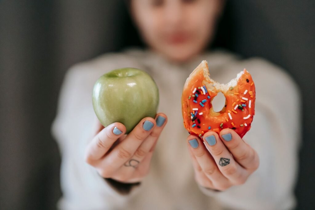 Crop anonymous female demonstrating delicious sweet donut and fresh green apple while making decision
