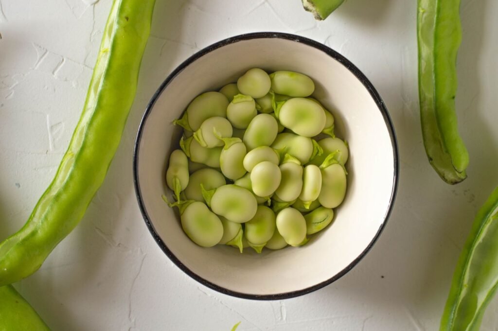 A top-down view of fresh broad beans in a bowl, showcasing their vibrant green color.