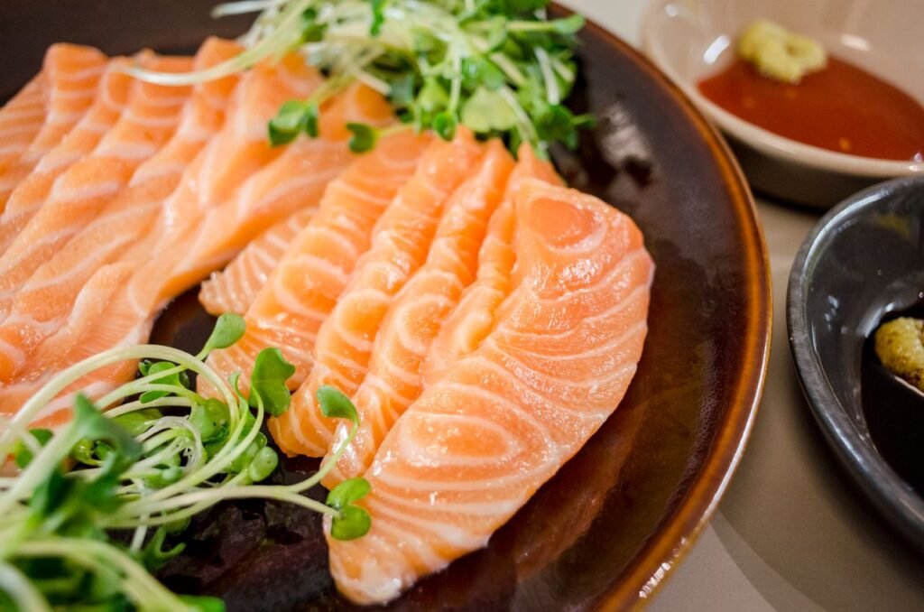 Delicious salmon sashimi served with fresh greens and dipping sauces on a plate.