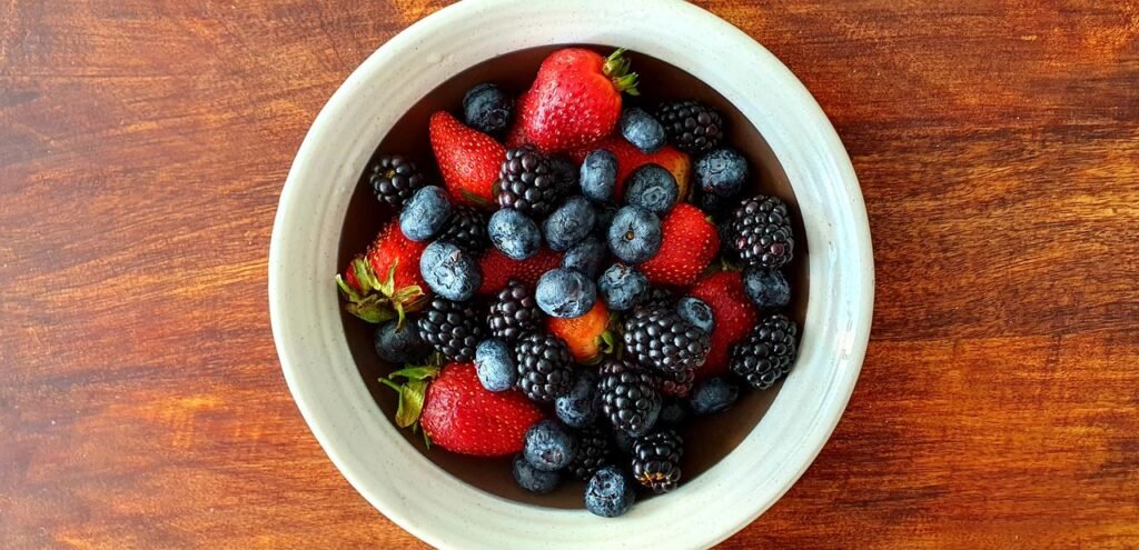 A vibrant assortment of strawberries, blackberries, and blueberries in a bowl on a wooden surface.
