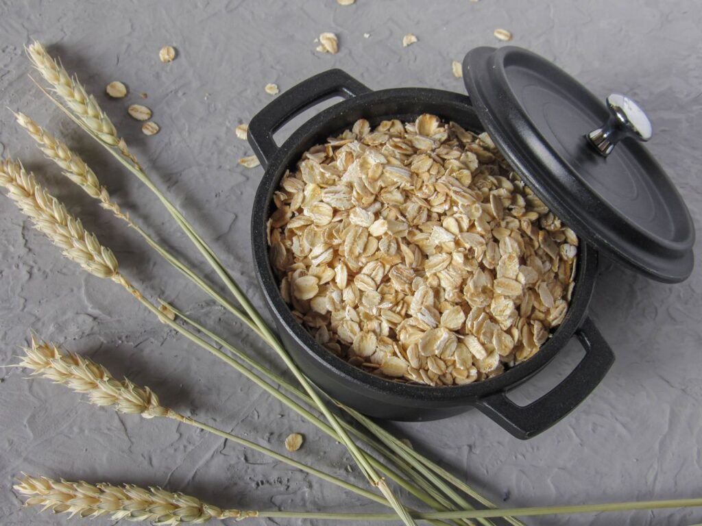 Flat lay of rolled oats in a black pot surrounded by wheat stalks on a textured surface.