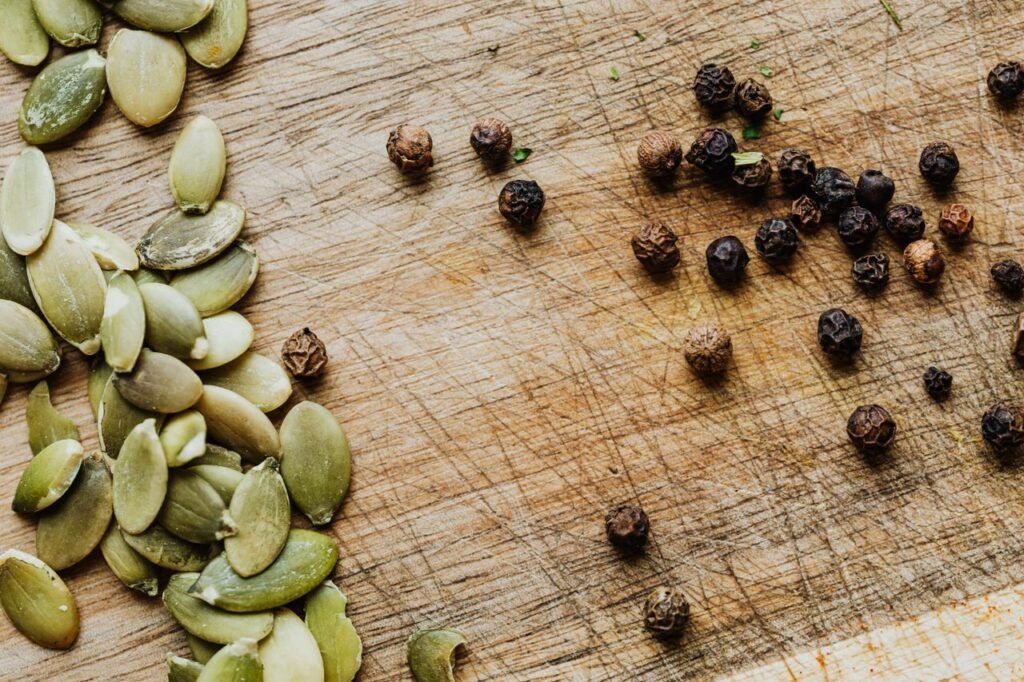 Close-up of pumpkin seeds and black peppercorns on a wooden cutting board.