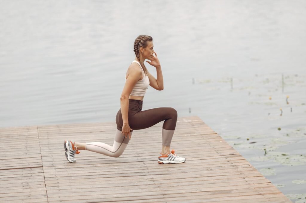 A woman performs lunges on a lakeside wooden deck, showcasing a fit lifestyle outdoors.
