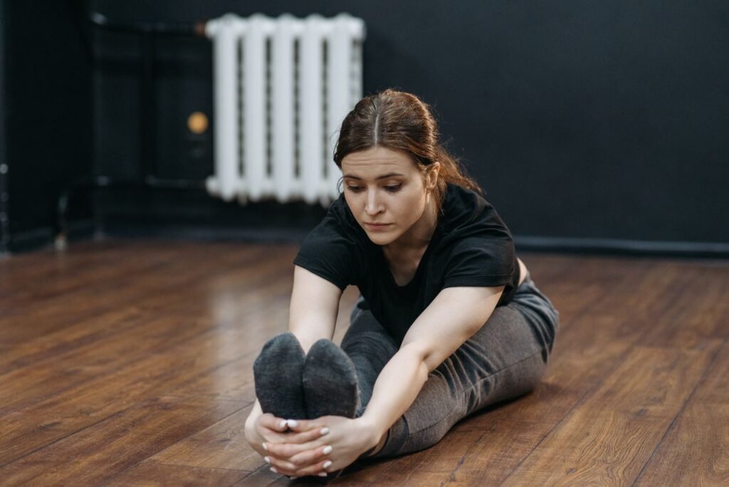Adult woman performing seated stretch indoors, focusing on flexibility and fitness.