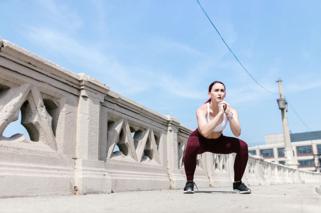 Woman performing a squat exercise outdoors beside a concrete railing under a clear sky.